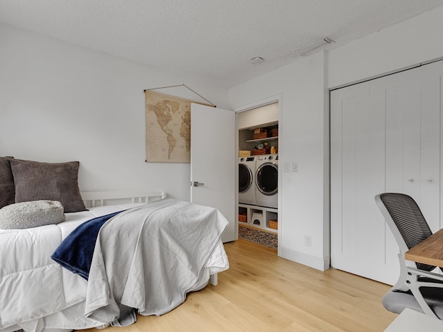 bedroom with a closet, a textured ceiling, light hardwood / wood-style floors, and washer and clothes dryer