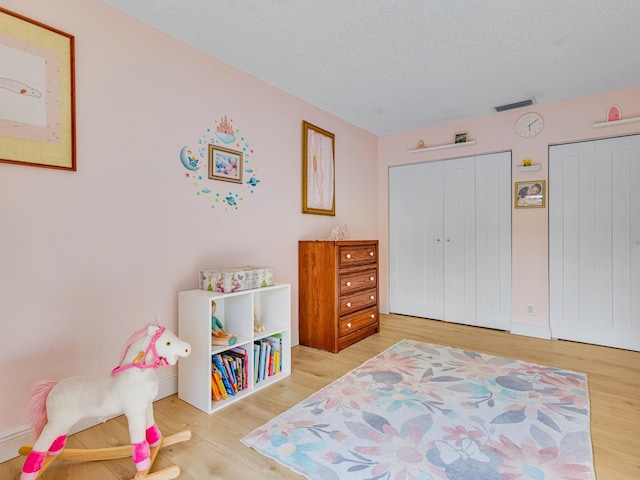 bedroom with a textured ceiling, light wood-type flooring, and multiple closets