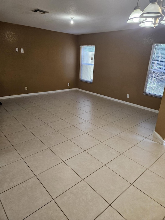 empty room featuring a notable chandelier and light tile patterned floors