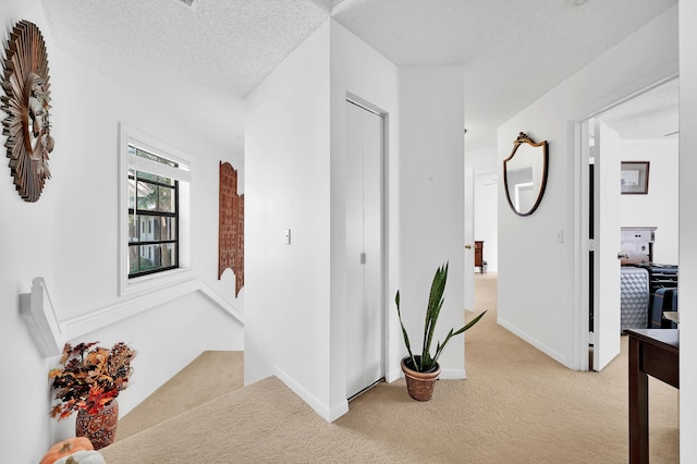 hall with light colored carpet and a textured ceiling