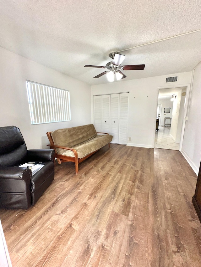 living room with a textured ceiling, light hardwood / wood-style flooring, and ceiling fan