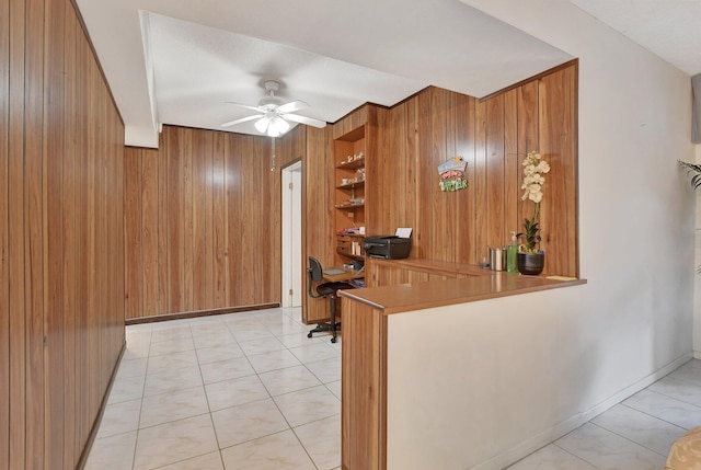 kitchen with kitchen peninsula, built in shelves, ceiling fan, wooden walls, and light tile patterned floors