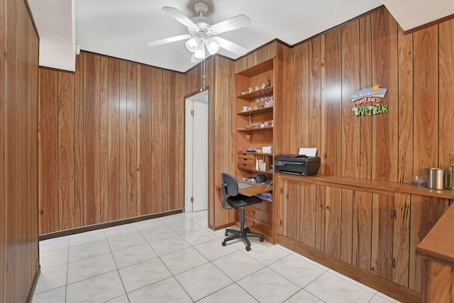 unfurnished office featuring ceiling fan, built in desk, a textured ceiling, and wooden walls