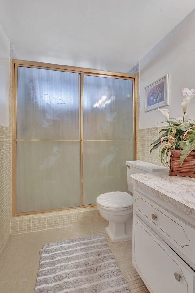 bathroom featuring tile patterned flooring, an enclosed shower, toilet, vanity, and tile walls