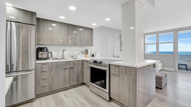 kitchen featuring sink, stainless steel appliances, light hardwood / wood-style flooring, kitchen peninsula, and a water view