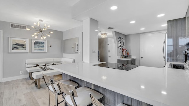 kitchen with kitchen peninsula, black electric cooktop, light hardwood / wood-style floors, and a notable chandelier