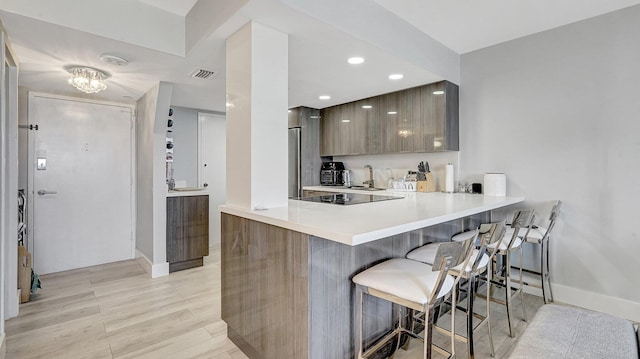 kitchen featuring a kitchen breakfast bar, light wood-type flooring, kitchen peninsula, and black electric cooktop