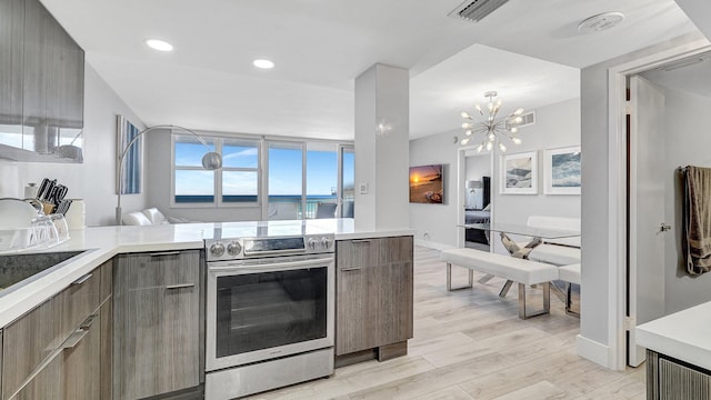 kitchen with kitchen peninsula, light wood-type flooring, stainless steel range with electric cooktop, and a notable chandelier