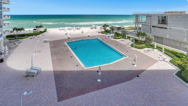 view of pool featuring a patio area, a water view, and a view of the beach