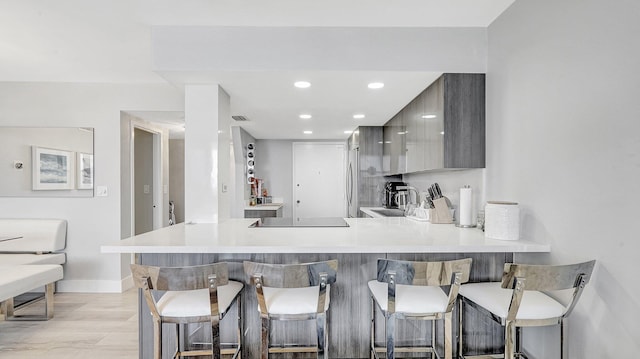 kitchen with kitchen peninsula, a breakfast bar, sink, gray cabinets, and light hardwood / wood-style floors