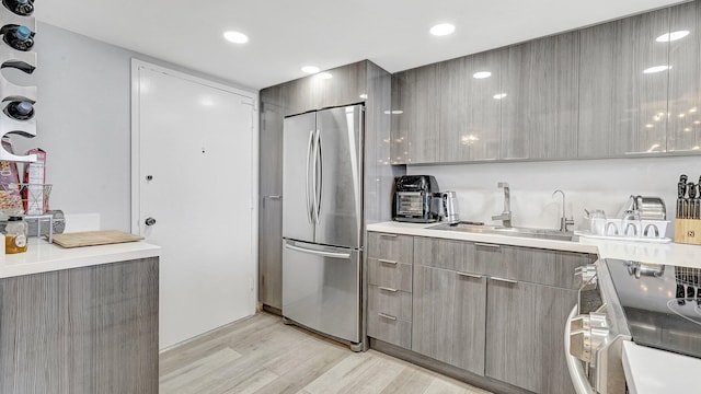 kitchen with stove, light hardwood / wood-style floors, stainless steel refrigerator, and sink