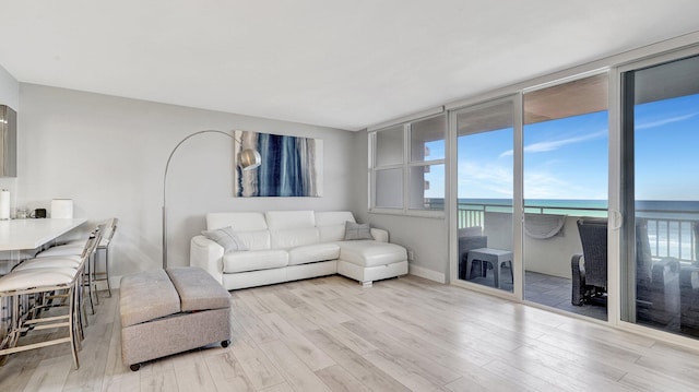 living room with light wood-type flooring, a water view, and expansive windows