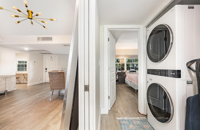 washroom with a chandelier, stacked washing maching and dryer, and light wood-type flooring