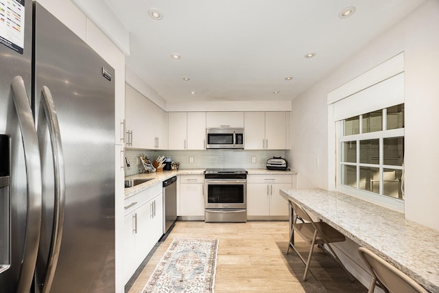 kitchen featuring stainless steel appliances, light stone counters, backsplash, white cabinets, and light wood-type flooring