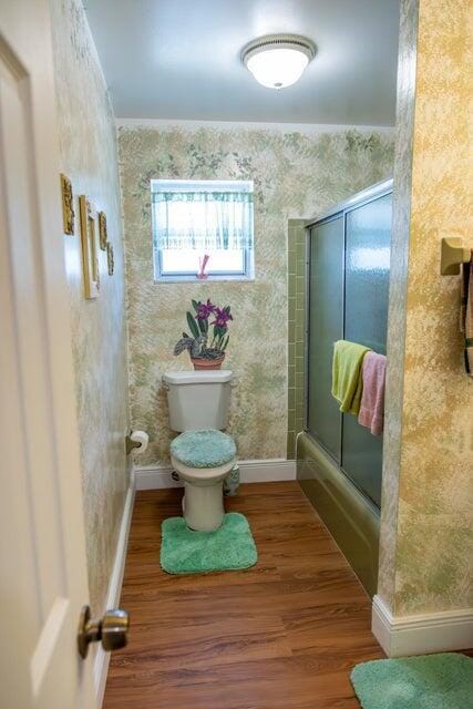 bathroom featuring hardwood / wood-style floors, combined bath / shower with glass door, and toilet