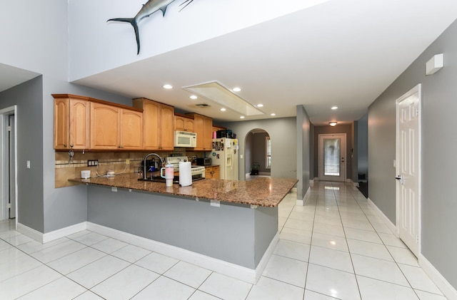 kitchen with kitchen peninsula, light tile patterned floors, white appliances, and dark stone counters