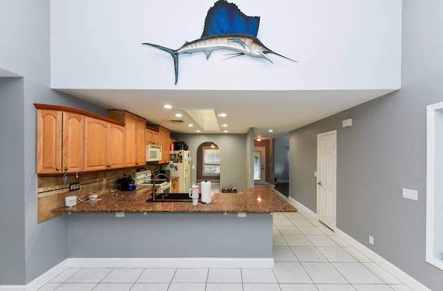 kitchen with white appliances, dark stone counters, light tile patterned floors, tasteful backsplash, and kitchen peninsula