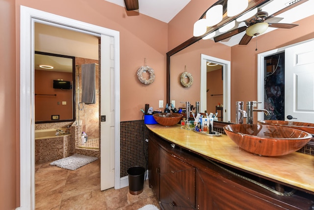 bathroom with tiled bath, ceiling fan, vanity, and tile walls