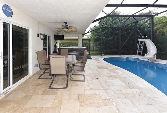 view of pool with glass enclosure, a water slide, ceiling fan, a patio, and a hot tub