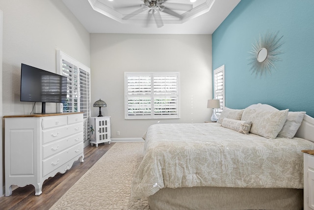 bedroom with ceiling fan, a raised ceiling, and dark wood-type flooring