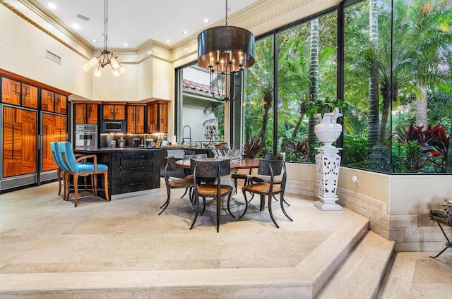 dining area with sink, a towering ceiling, ornamental molding, and a chandelier