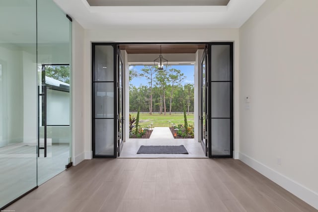 doorway featuring a tray ceiling, french doors, light wood-type flooring, and a notable chandelier