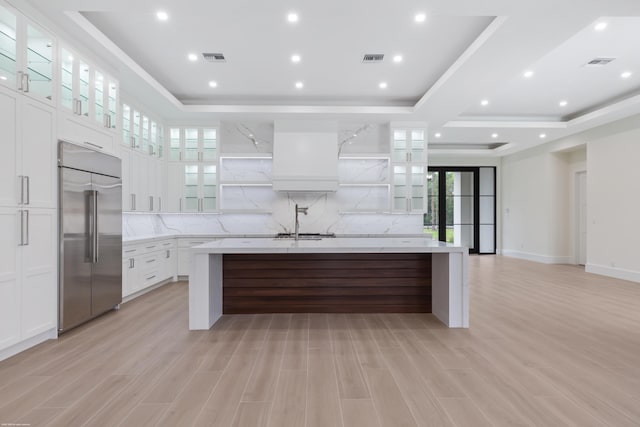 kitchen featuring white cabinets, a tray ceiling, stainless steel built in fridge, and an island with sink