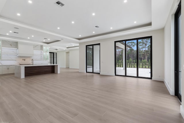 unfurnished living room with sink, light hardwood / wood-style flooring, and a tray ceiling