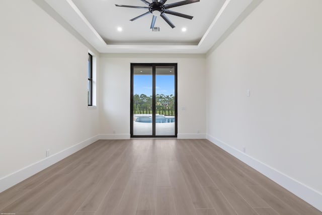 spare room with a wealth of natural light, a raised ceiling, light hardwood / wood-style flooring, and ceiling fan