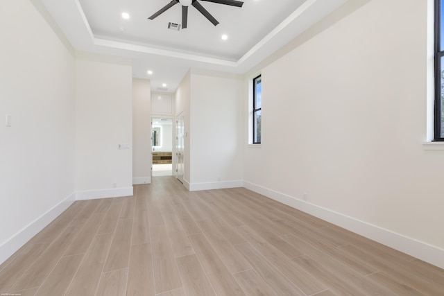 unfurnished room featuring light wood-type flooring, a tray ceiling, and ceiling fan