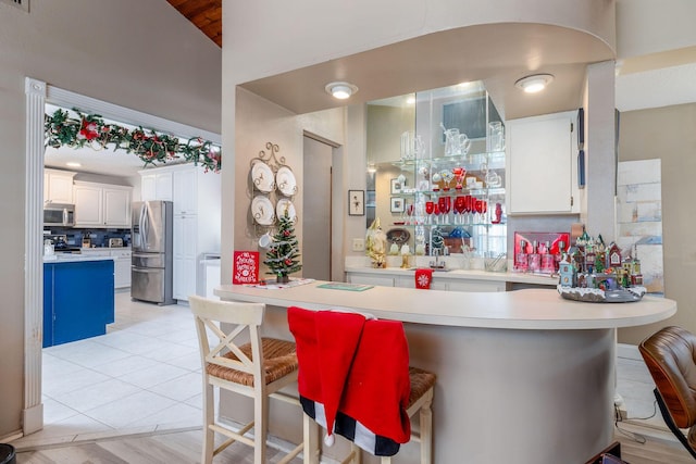 kitchen featuring lofted ceiling, kitchen peninsula, appliances with stainless steel finishes, a kitchen bar, and white cabinetry