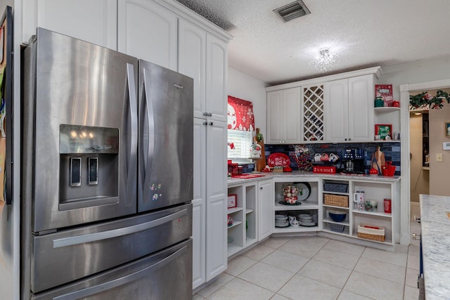 kitchen with white cabinets, stainless steel fridge, a textured ceiling, and light tile patterned floors