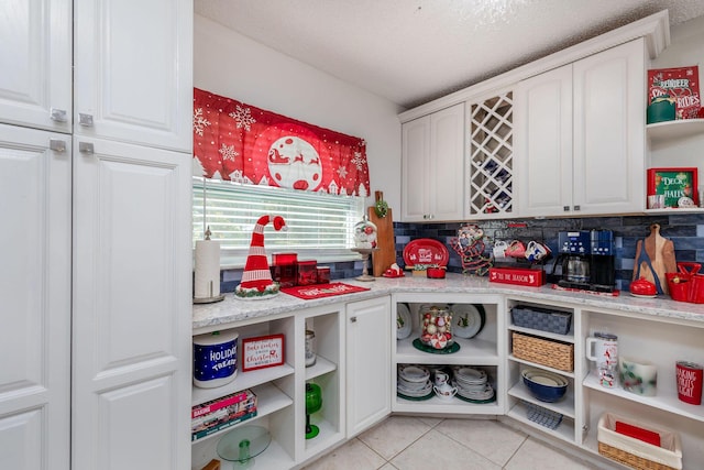 kitchen featuring white cabinetry, light stone counters, backsplash, a textured ceiling, and light tile patterned floors