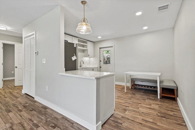 kitchen with white cabinets, dark hardwood / wood-style flooring, kitchen peninsula, and stainless steel refrigerator