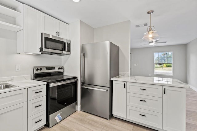 kitchen featuring kitchen peninsula, appliances with stainless steel finishes, pendant lighting, white cabinets, and light hardwood / wood-style floors