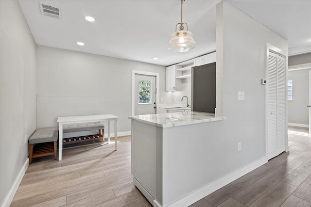 kitchen featuring white cabinets, stainless steel fridge, light hardwood / wood-style floors, and kitchen peninsula