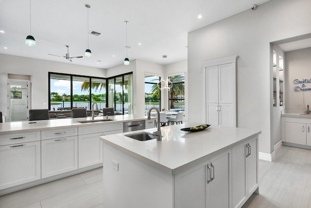 kitchen with sink, white cabinets, decorative light fixtures, and a center island with sink