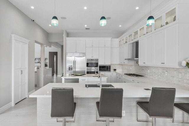 kitchen featuring built in appliances, wall chimney range hood, hanging light fixtures, and a breakfast bar area