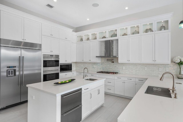 kitchen with built in appliances, white cabinetry, sink, and wall chimney exhaust hood