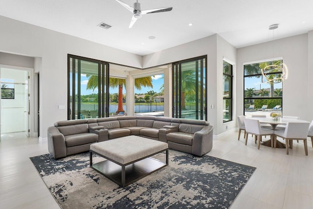 living room with ceiling fan, a water view, and a healthy amount of sunlight