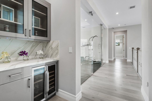 bar with backsplash, wine cooler, light stone counters, and light wood-type flooring