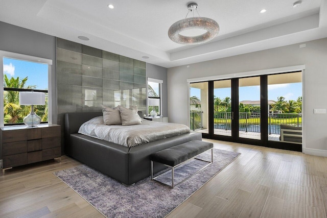 bedroom with a raised ceiling, a water view, and multiple windows