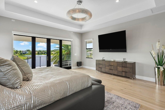 bedroom with access to outside, a tray ceiling, and light hardwood / wood-style floors