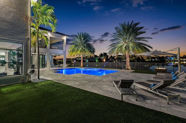 pool at dusk with a yard, a patio, and pool water feature