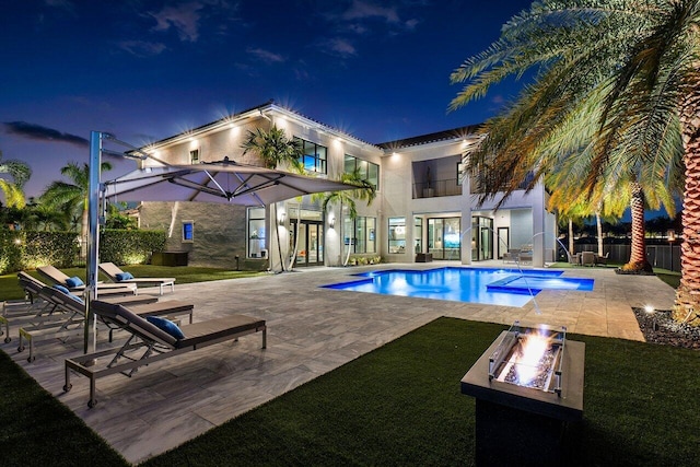 pool at twilight with a patio area and a fire pit