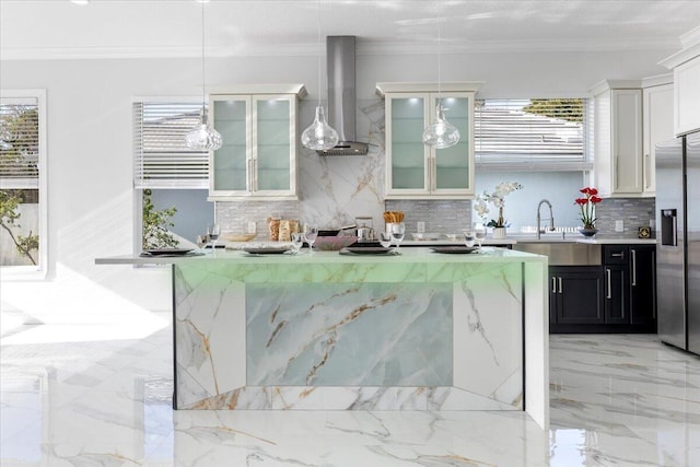 kitchen with a wealth of natural light, hanging light fixtures, wall chimney range hood, and stainless steel refrigerator with ice dispenser