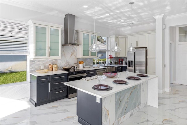 kitchen featuring wall chimney range hood, a kitchen island, pendant lighting, white cabinets, and appliances with stainless steel finishes