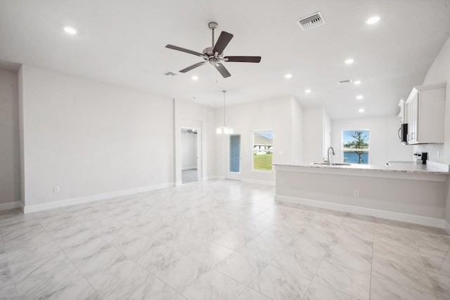 unfurnished living room featuring ceiling fan with notable chandelier and sink