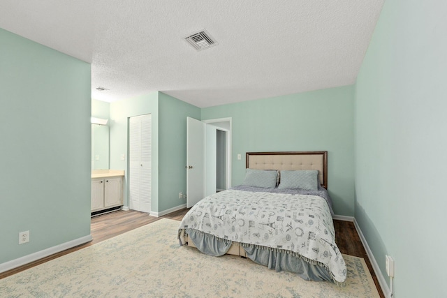 bedroom featuring hardwood / wood-style floors, a closet, a textured ceiling, and ensuite bath