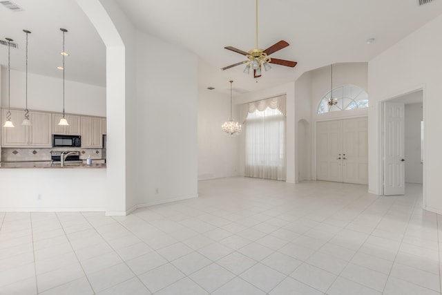 unfurnished living room featuring ceiling fan with notable chandelier, light tile patterned floors, and a high ceiling